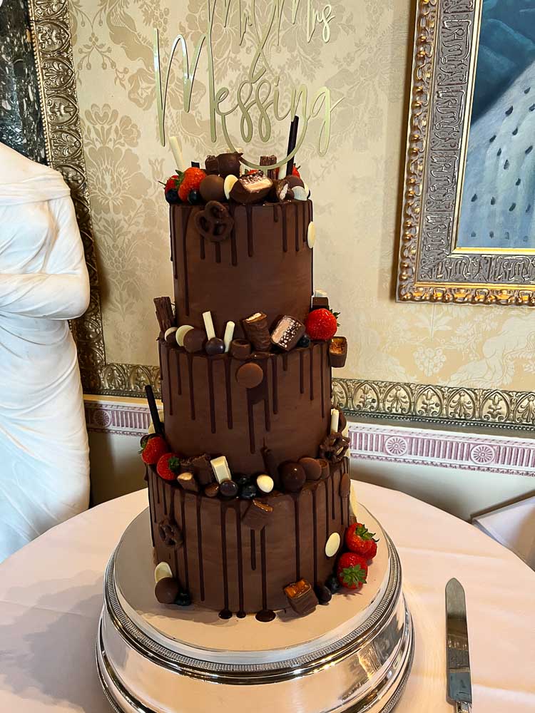 Three-tier chocolate drip wedding cake decorated with chocolates and strawberries at Brocket Hall