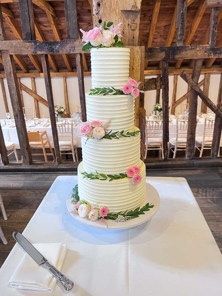 Four-tier white wedding cake decorated with pink roses and greenery at Tewinbury Farm Hotel