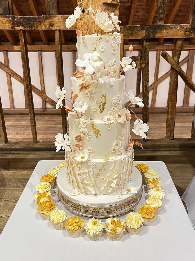 Four-tier white wedding cake with gold details and delicate white sugar flowers at Tewinbury Farm Hotel