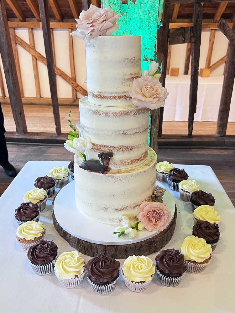 Three-tier semi-naked wedding cake with blush pink flowers and cupcakes at Tewinbury